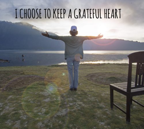 Inspirational quote - I choose to keep a grateful heart. With woman standing alone, hands raise with open arms against nature lake background in the morning. Gratitude concept.